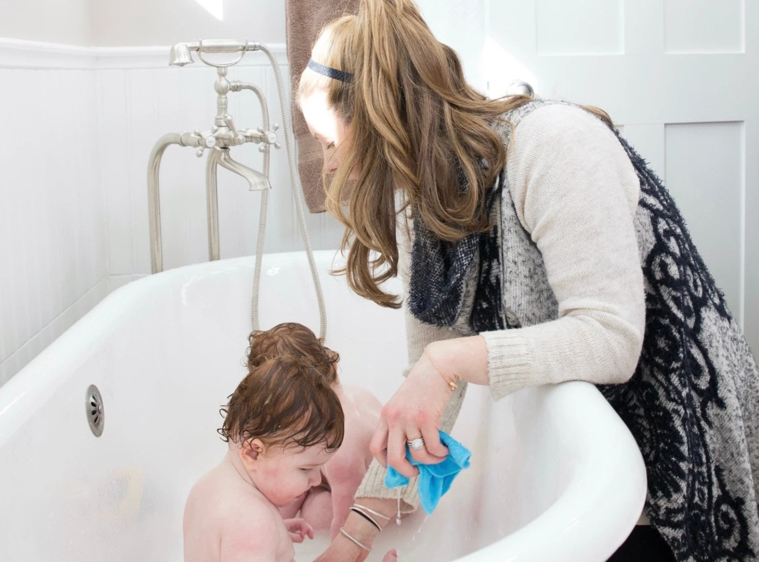 An adult bathing a child at the side of a tub.